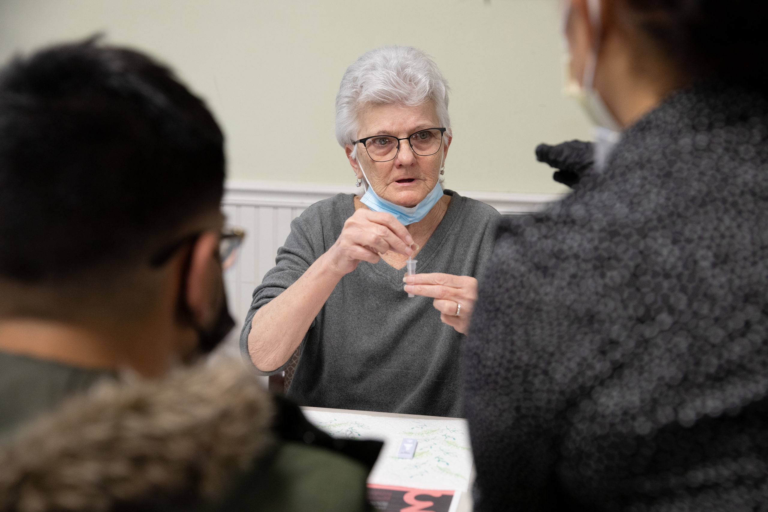 An older adult holding a vial from a COVID-19 rapid test with a couple of onlookers.