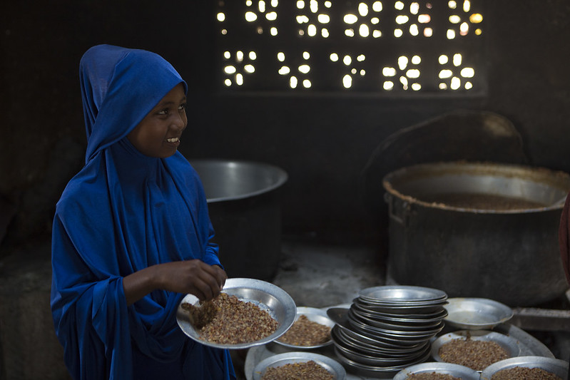 Female Somali student in blue holding a plate of food, smiling at someone off camera