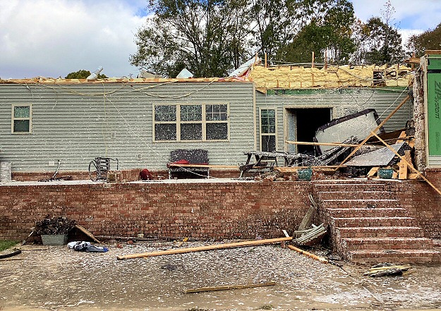 House showing structural damage to the roof, siding, windows and doors from a tornado