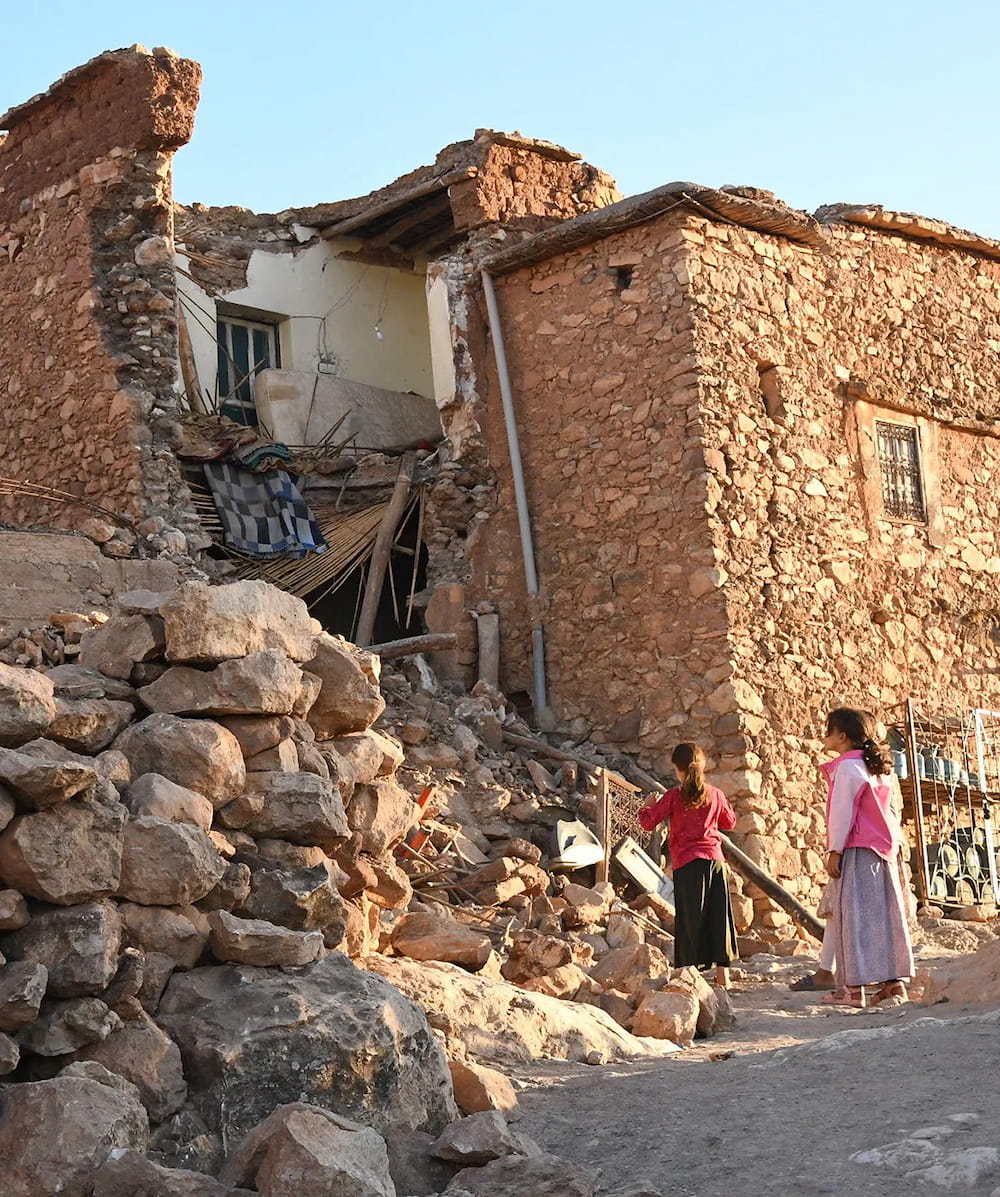 Image of partially collapsed building with two female children looking at the rubble
