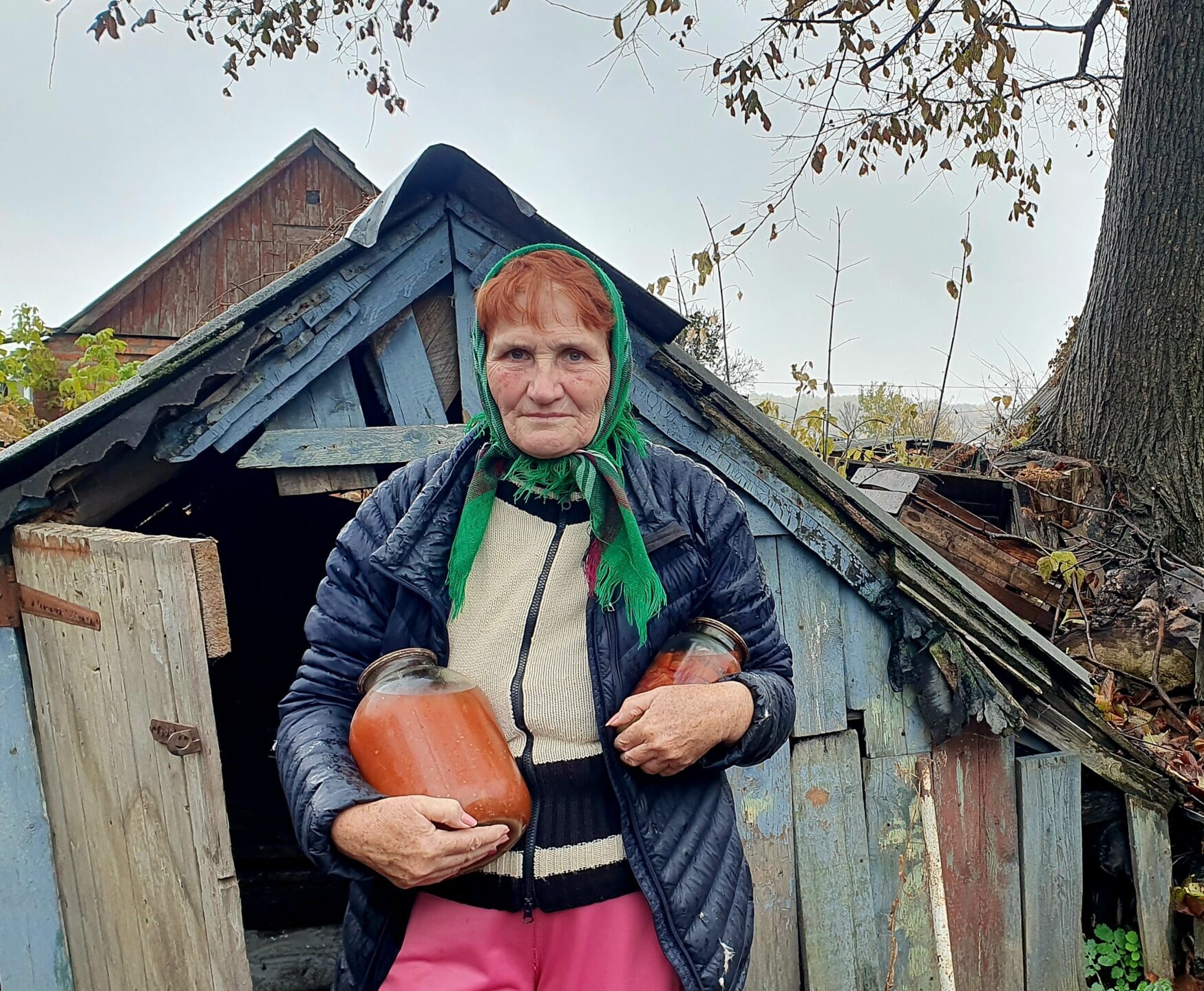 A woman holding jars of food stands in front of the entrance to a cellar