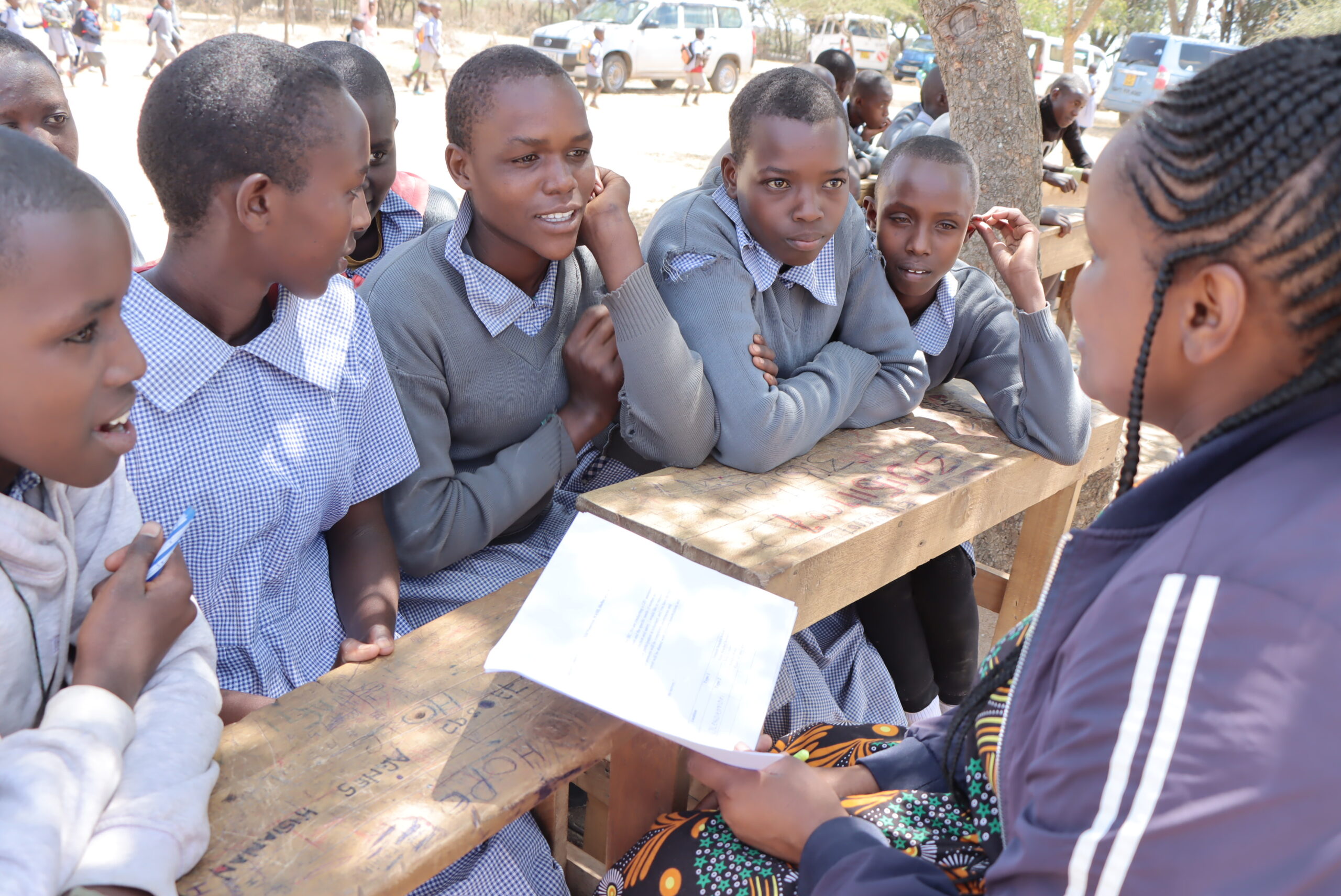 Primary school girls sit at a table across from a woman holding a notebook